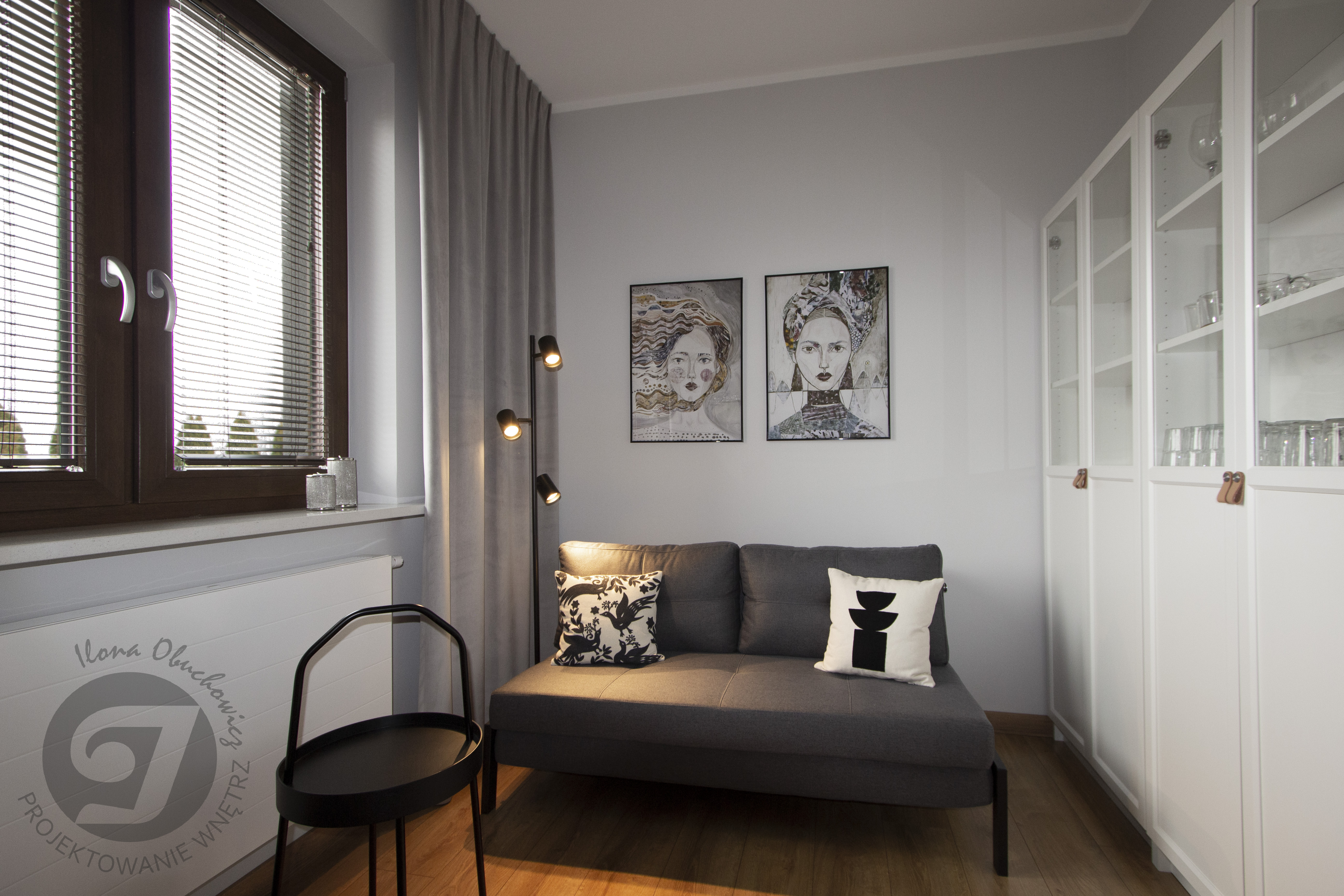 pokój gościnny, z małą rozkładaną kanapą, regały białe Billy Ikea, przeszklone fronty ze skórzanymi uchwytami, grafiki z portretami kobiet w czarnej ramie 